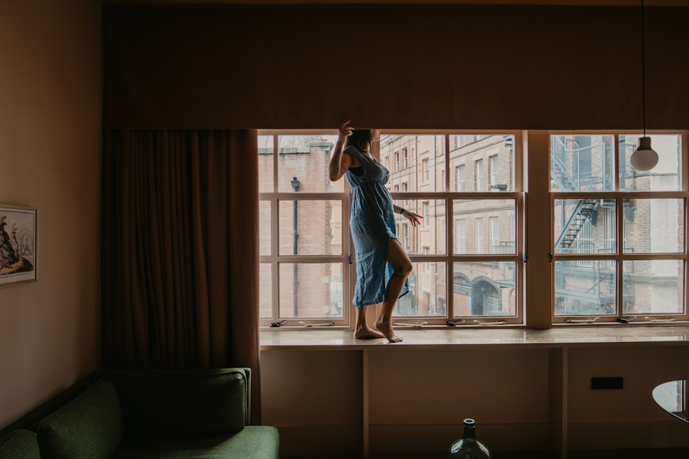 woman in blue dress standing near window