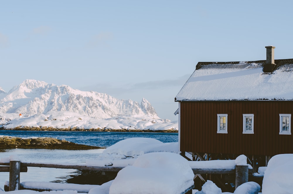 a house is covered in snow next to a body of water