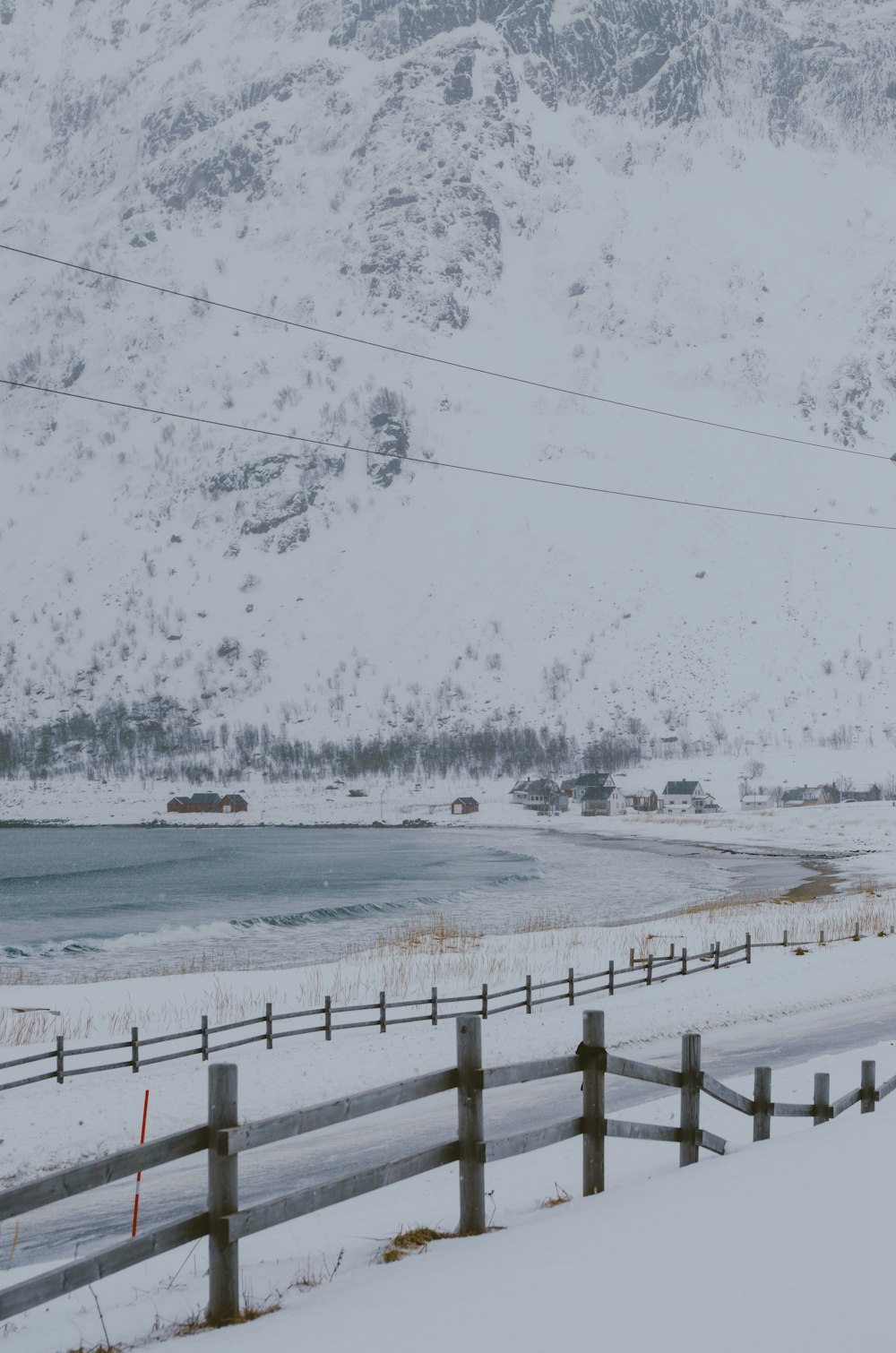 a snow covered field with a fence and mountains in the background