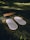 A set of white acupressure mats with spikes rests on a green cloth, placed on a grassy field. Adjacent to them, there is a rectangular wooden block with a design engraved on it.