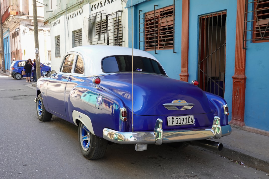 blue and white vintage car parked beside white concrete building during daytime