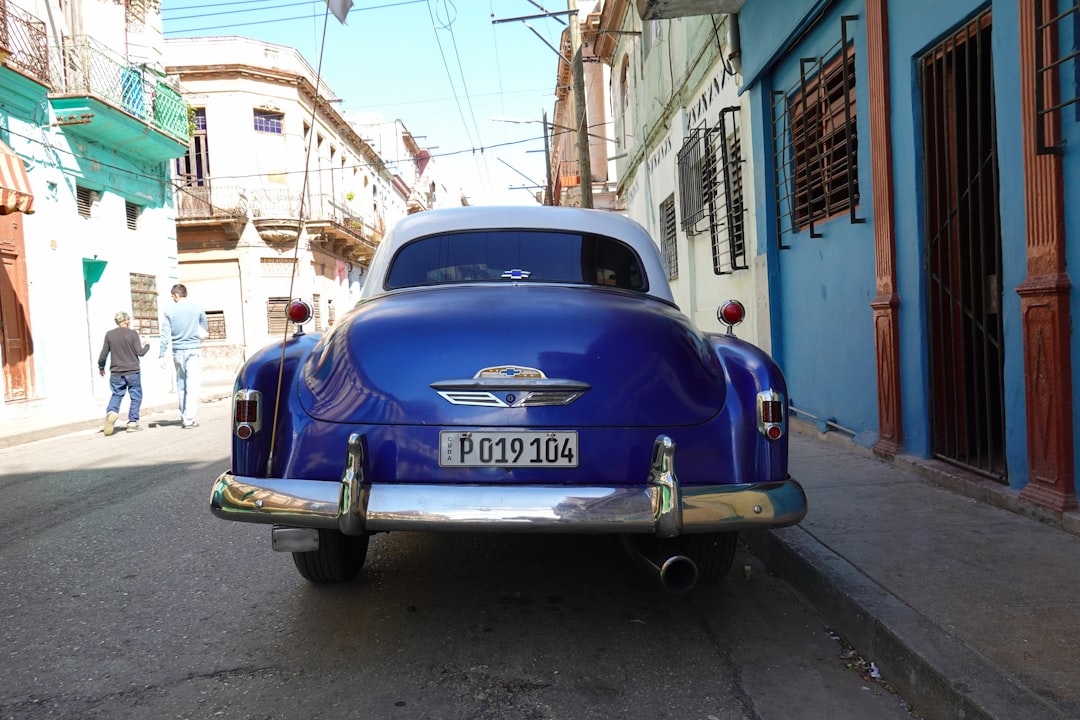 blue car parked beside white concrete building during daytime