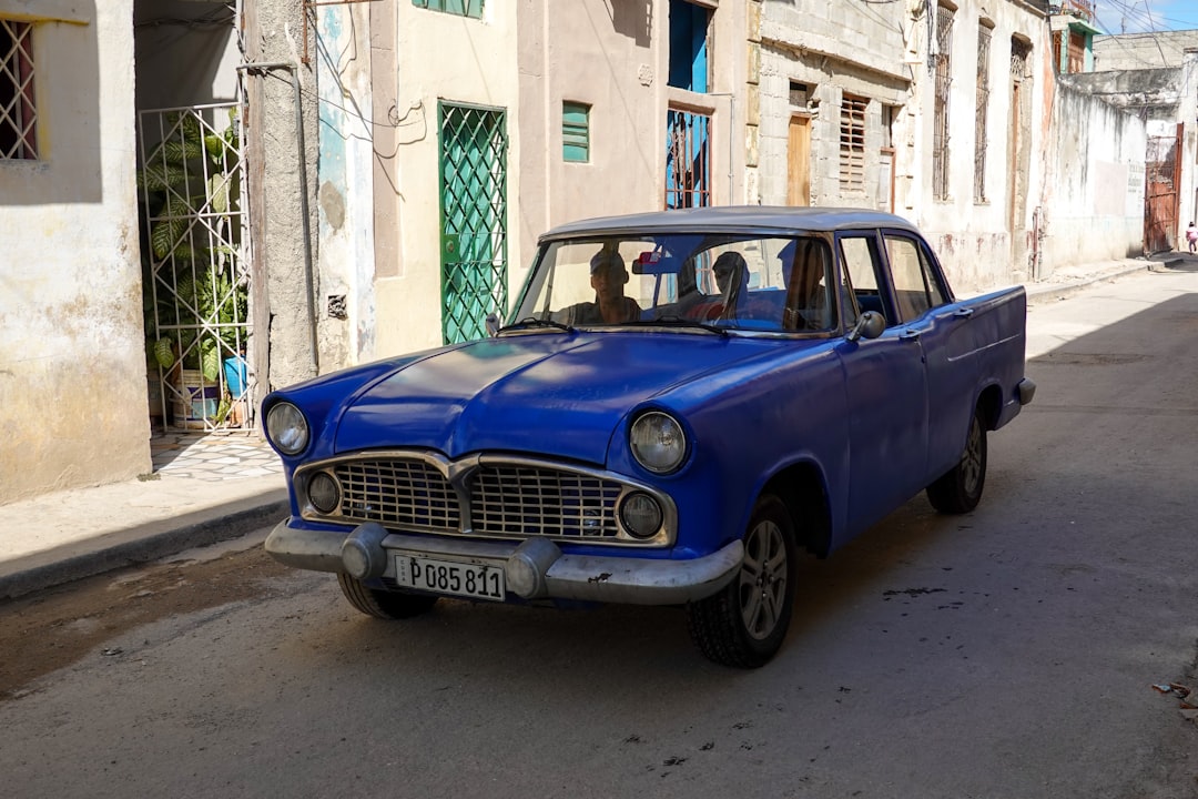 blue classic car parked beside white concrete building during daytime