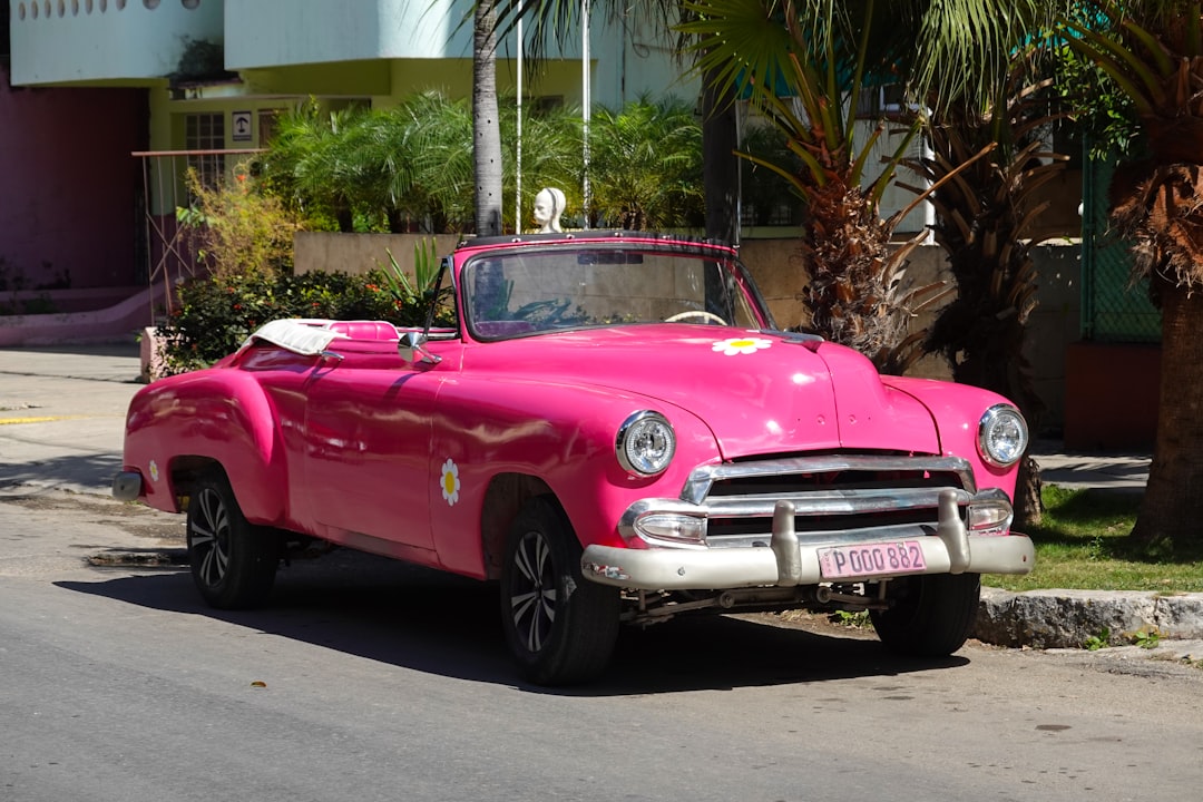 pink vintage car parked near palm tree during daytime