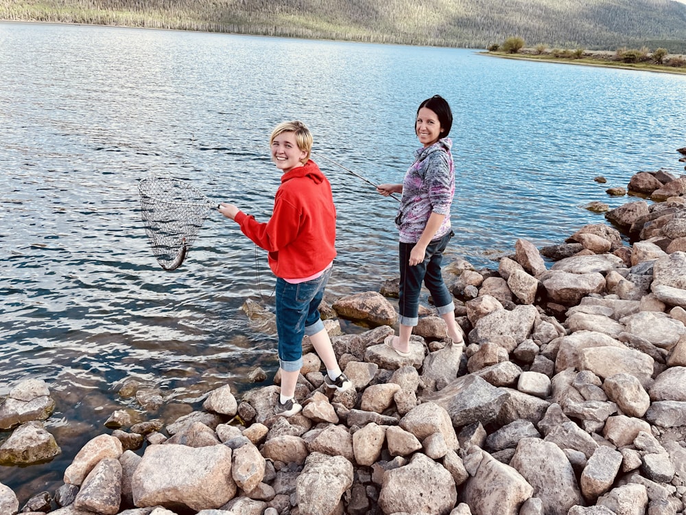 boy in red t-shirt and blue denim shorts standing on rocky shore during daytime