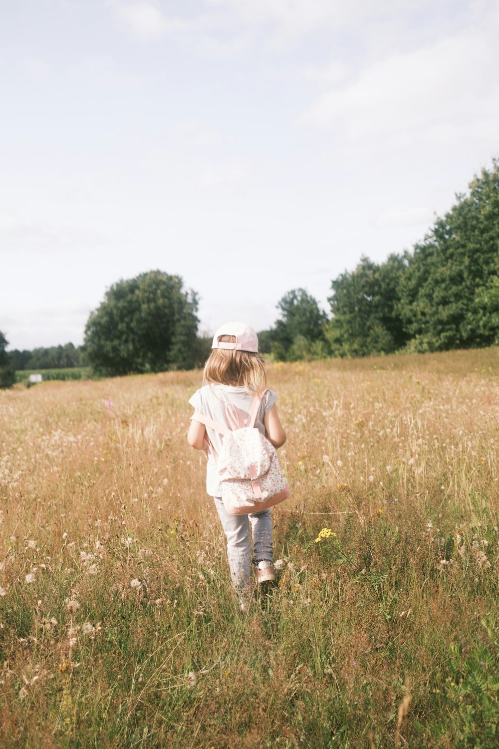 a little girl walking through a field of tall grass