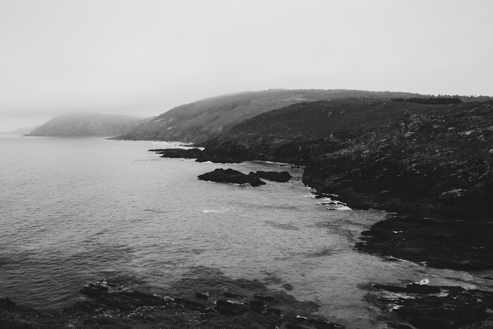 Foto en escala de grises de una montaña cerca del cuerpo de agua