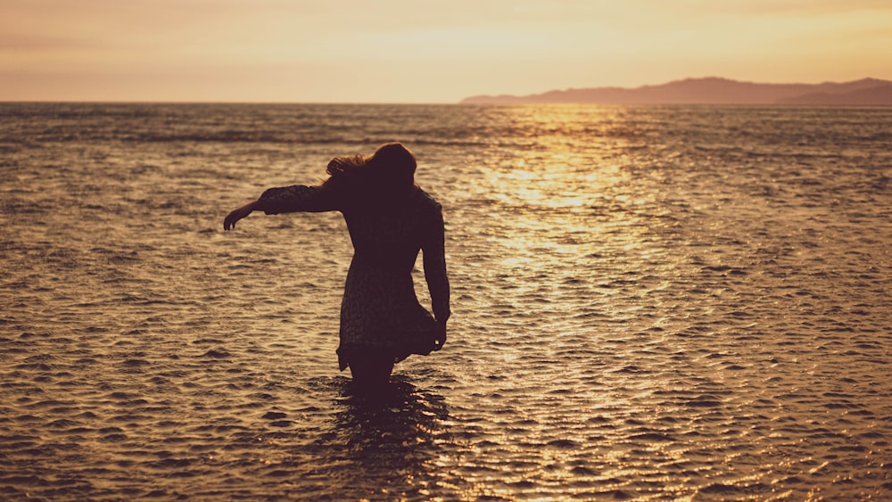 silhouette of man standing on water during sunset