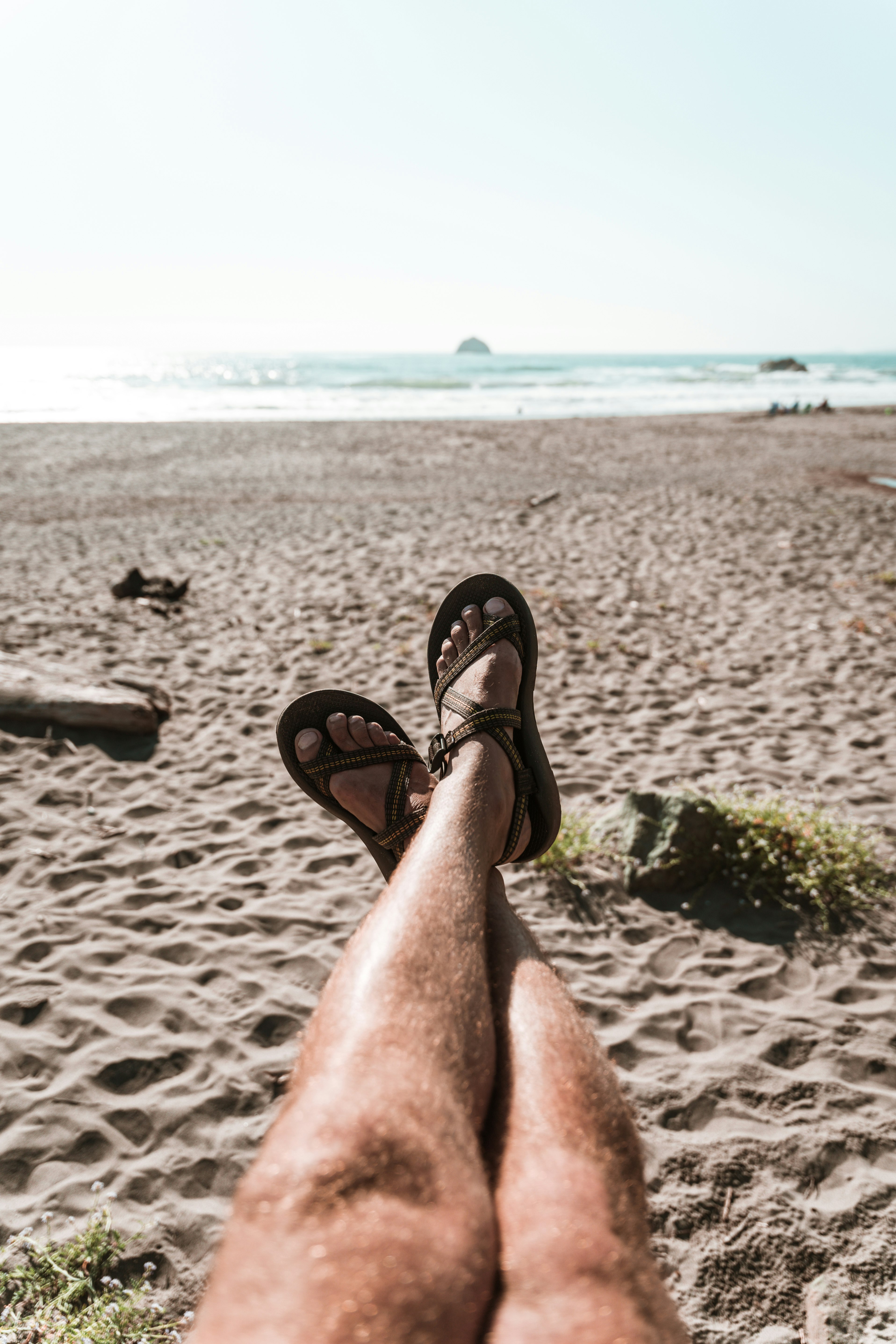 person wearing black flip flops sitting on gray sand during daytime