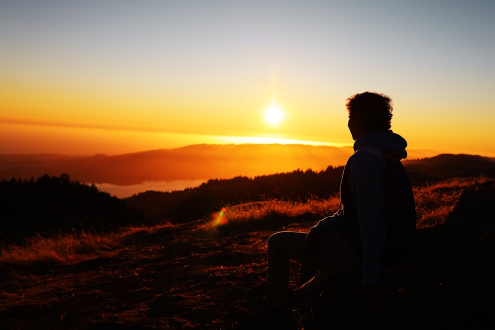 silhouette of man sitting on rock during sunset