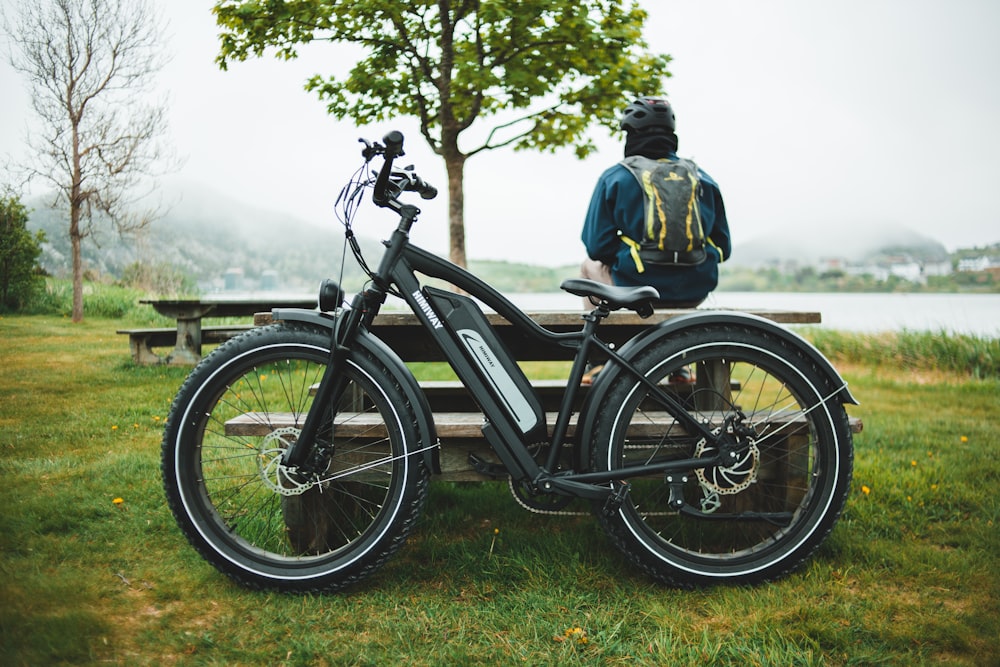 man in blue jacket and black backpack riding on black bicycle on green grass field during