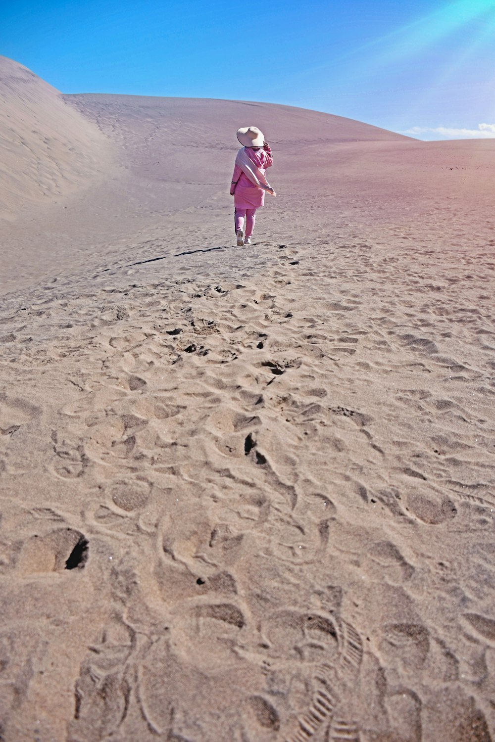 girl in pink jacket and pink pants walking on sand