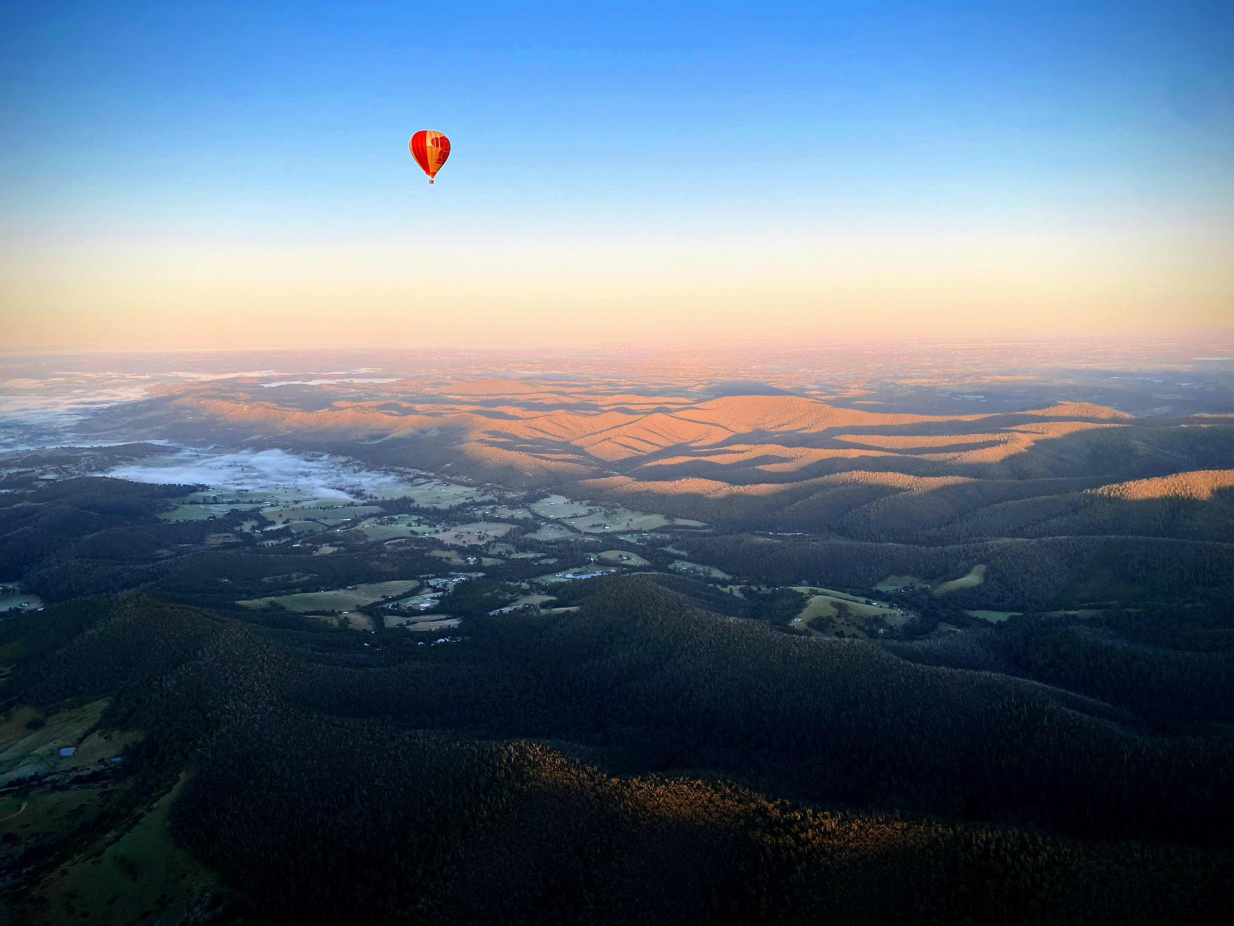 red hot air balloon flying over green field during daytime
