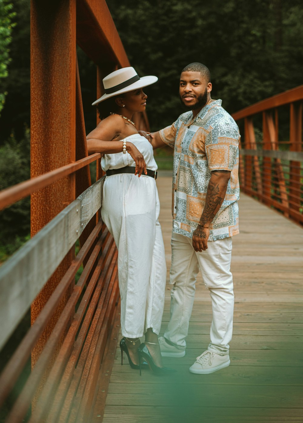 man in white pants and woman in white dress walking on wooden bridge during daytime