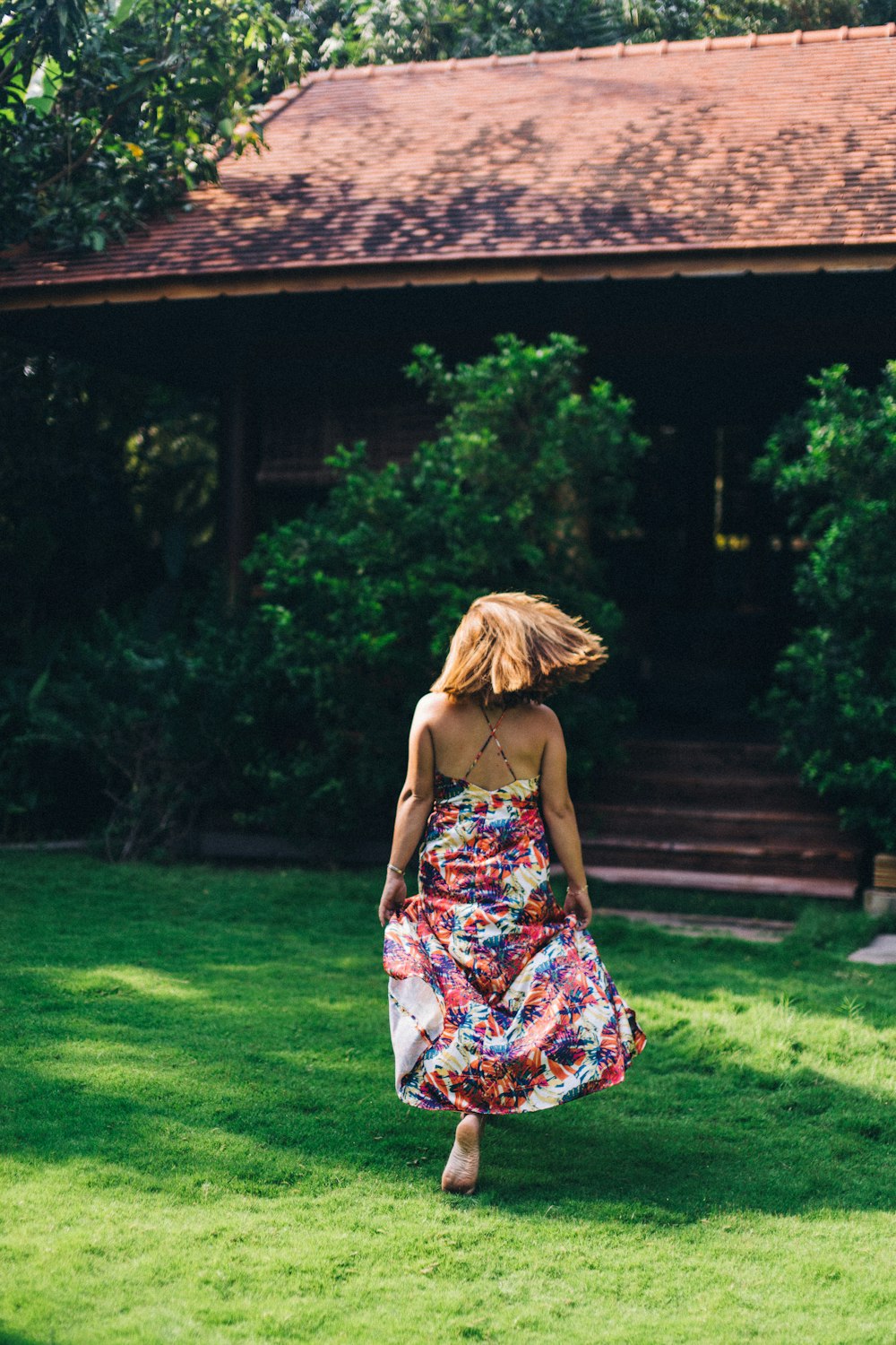 woman in blue and red floral spaghetti strap dress standing on green grass field during daytime