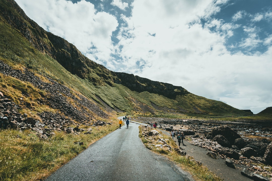 person walking on gray asphalt road near green mountain under white clouds during daytime