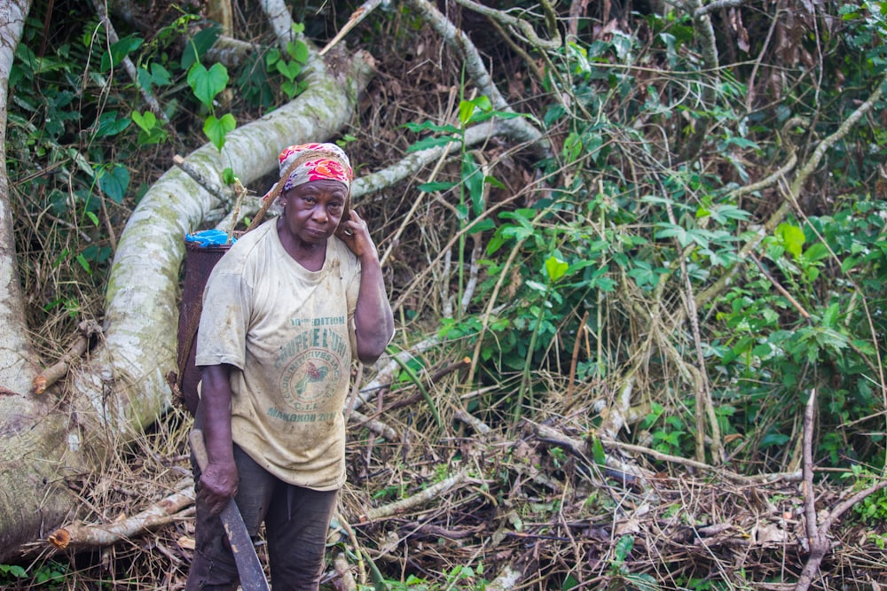 Hombre con camiseta marrón de cuello redondo y pantalones negros sentado en un tronco de árbol