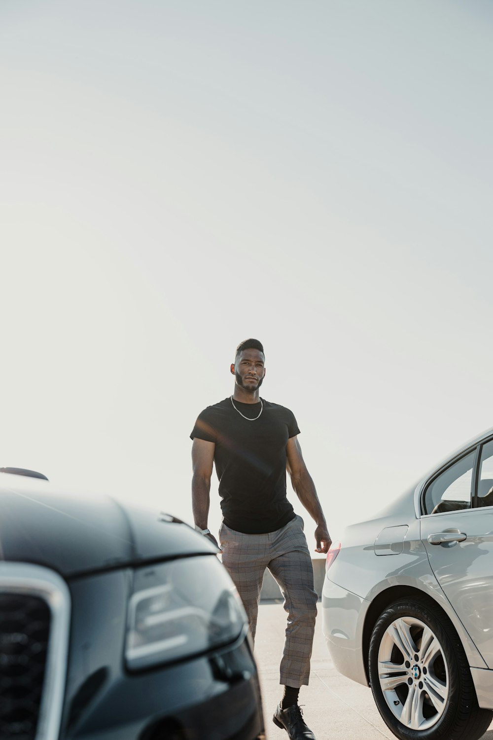 man in black tank top and white pants standing beside silver car