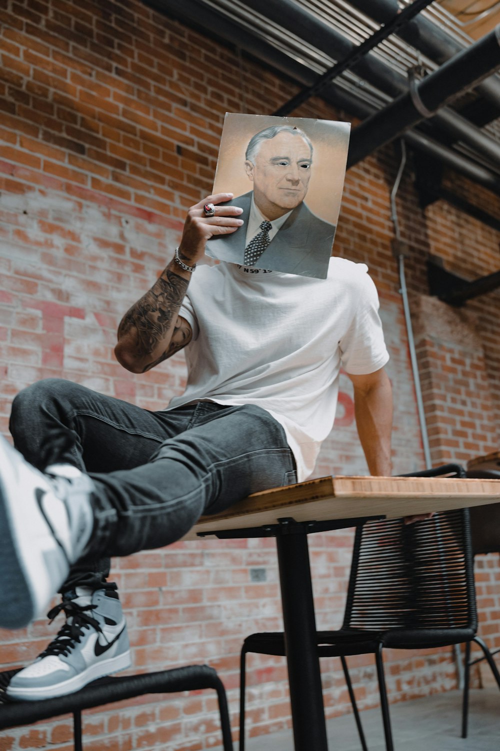 man in white crew neck t-shirt and blue denim jeans sitting on brown wooden bench