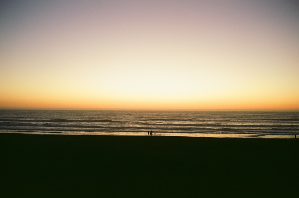 silhouette of person standing on seashore during sunset