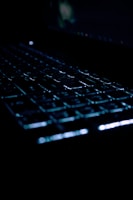 A close-up of a stylish computer keyboard with glowing keys in a dark room.