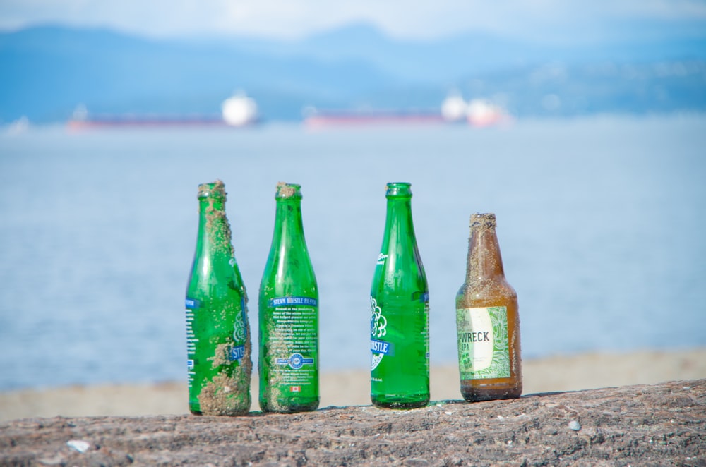 three green glass bottles on brown sand during daytime