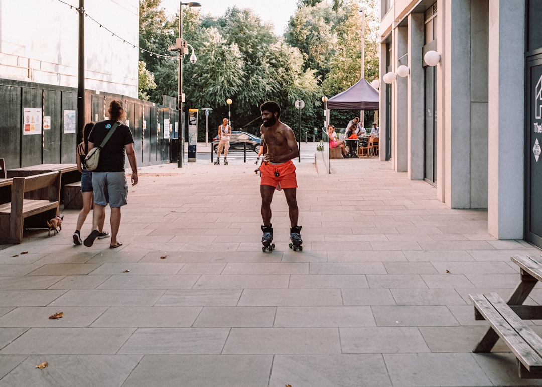 man in red t-shirt and black shorts walking on sidewalk during daytime