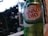 A can of Canada Dry ginger ale is prominently displayed in the foreground with condensation droplets visible on its surface. It features a green, gold, and red label. The background shows a blurred view of trees and possibly a window frame, suggesting an outdoor or patio setting.