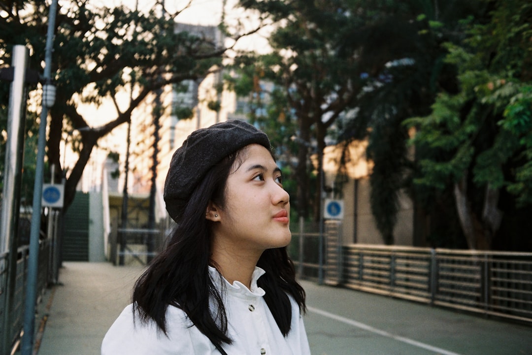 woman in white button up shirt and black knit cap standing on sidewalk during daytime