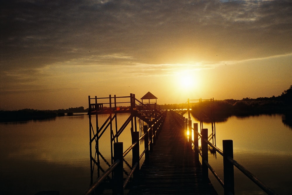 silhouette of wooden dock on body of water during sunset