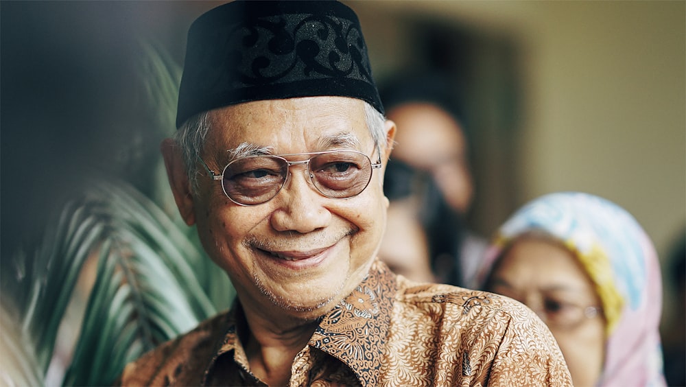 smiling woman in brown and beige floral shirt wearing black framed eyeglasses