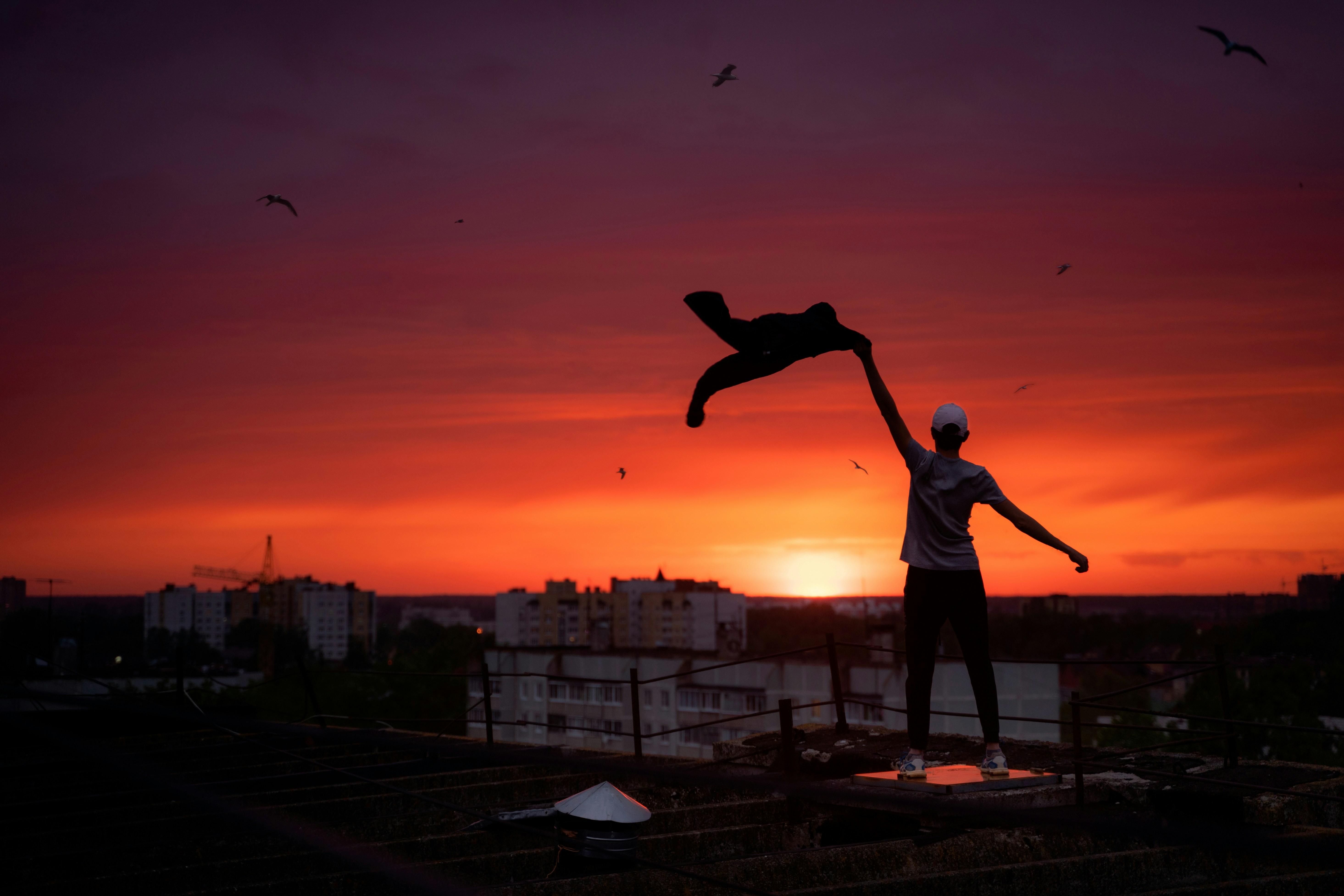 man in blue t-shirt and black shorts standing on roof top during sunset