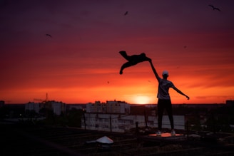 man in blue t-shirt and black shorts standing on roof top during sunset