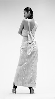 A model posing in a sleek, structured black dress with subtle rose accents, framed by large white negative space.