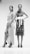 Two women stand confidently in intricate, patterned dresses and high heels. One dress features wrap elements with a high slit, while the other is adorned with a large white belt. The setting is minimal, enhancing the focus on their fashion and stance.