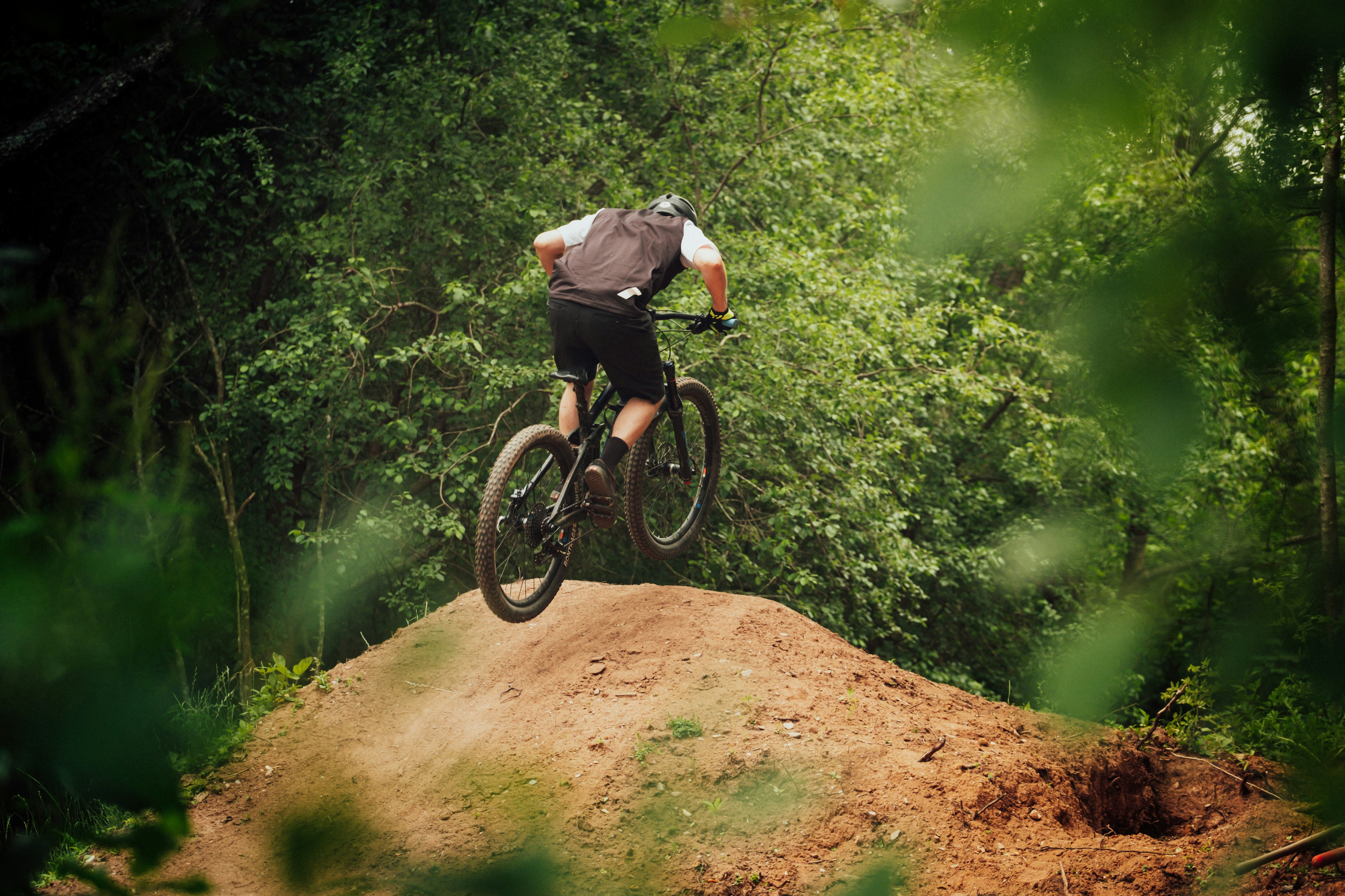 man in black jacket riding black mountain bike on brown dirt road between green trees during