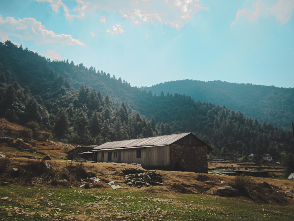 casa di legno marrone sul campo di erba verde vicino agli alberi verdi e alle montagne durante il giorno