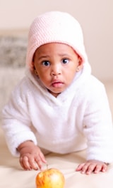 A baby wearing a white outfit adorned with small blue patterns and a matching hat is lying on a fluf