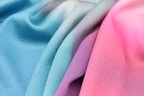 Soft, textured fabric draped in smooth folds, showcasing a gradient of soothing pastel colors, ranging from blue and teal to pink and lilac.