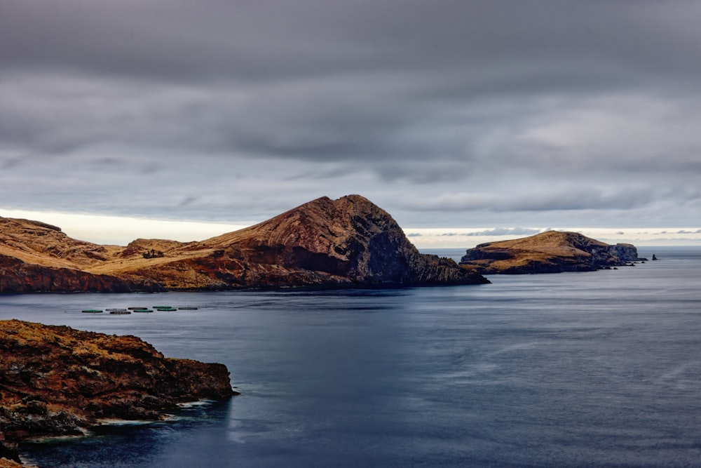 brown rocky mountain beside body of water under cloudy sky during daytime