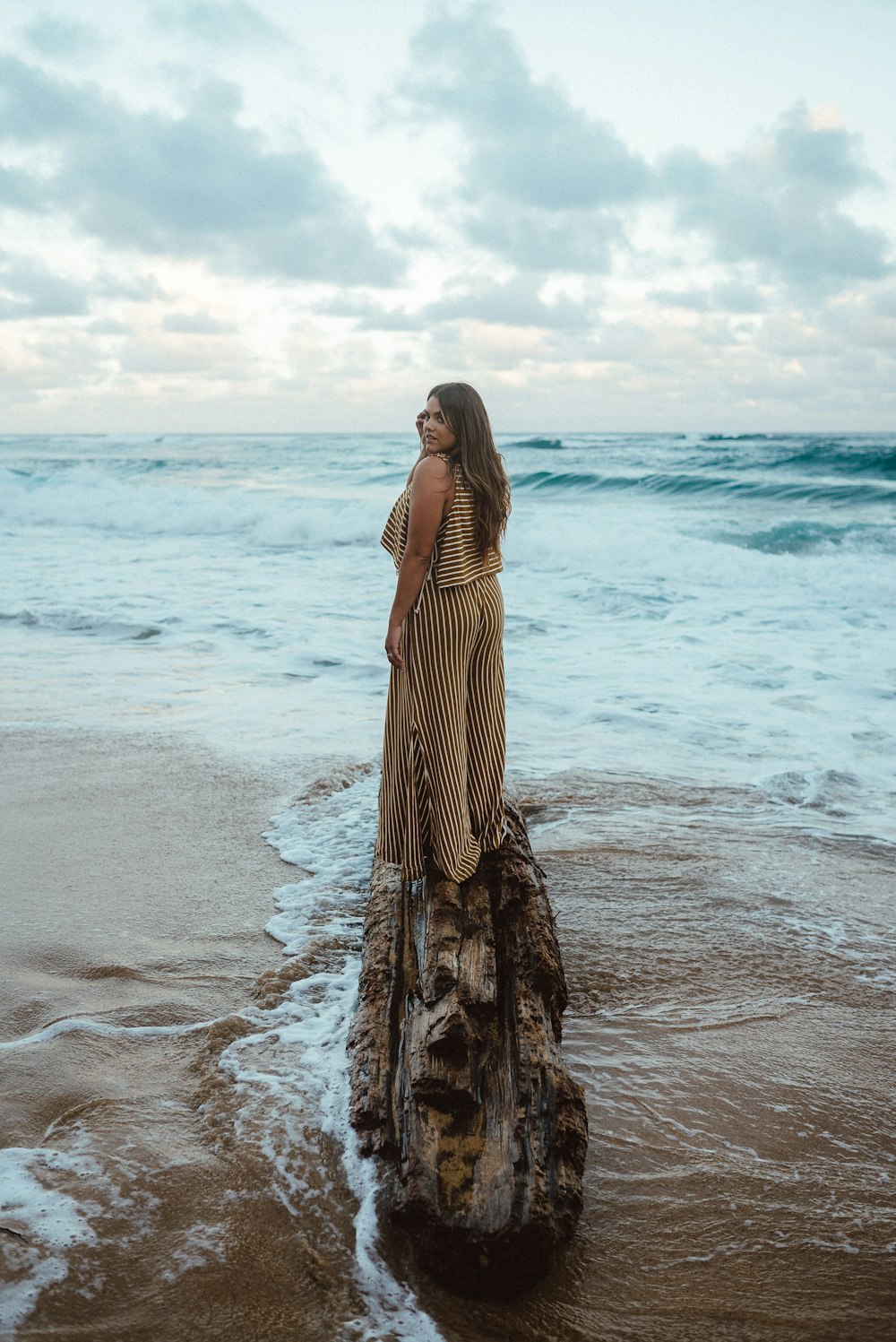 Mujer en vestido de rayas marrones y blancas de pie en la playa durante el día