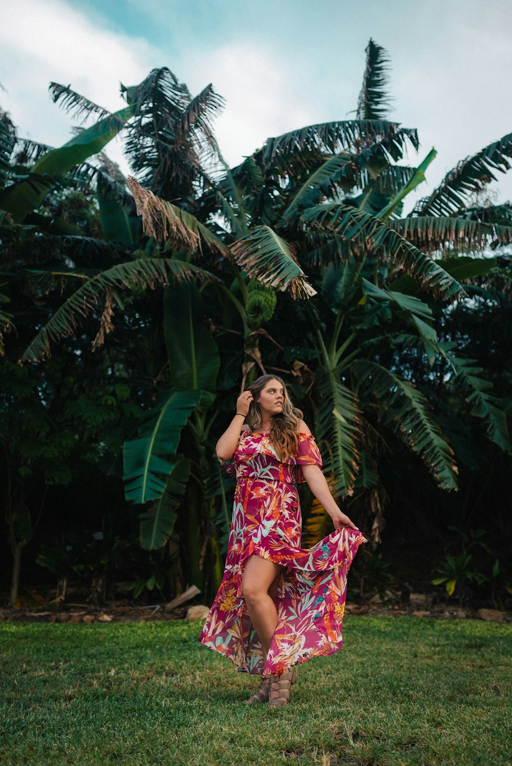 woman in purple and white floral dress standing near green palm tree during daytime