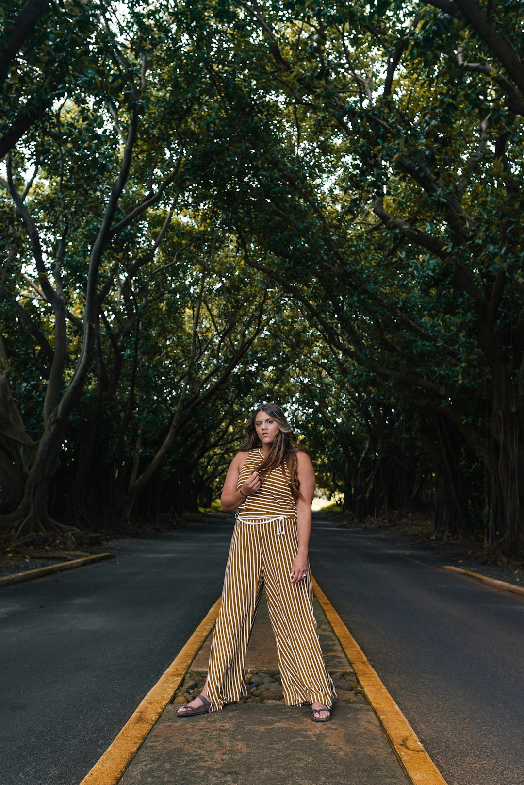 woman in brown dress standing on road between trees during daytime