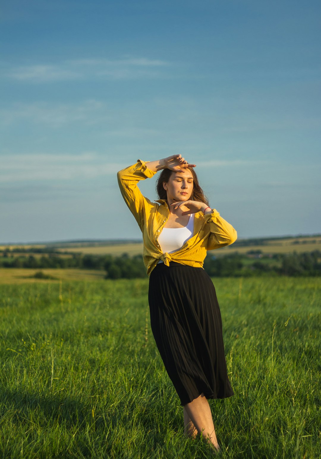 woman in yellow long sleeve shirt and black skirt standing on green grass field under blue