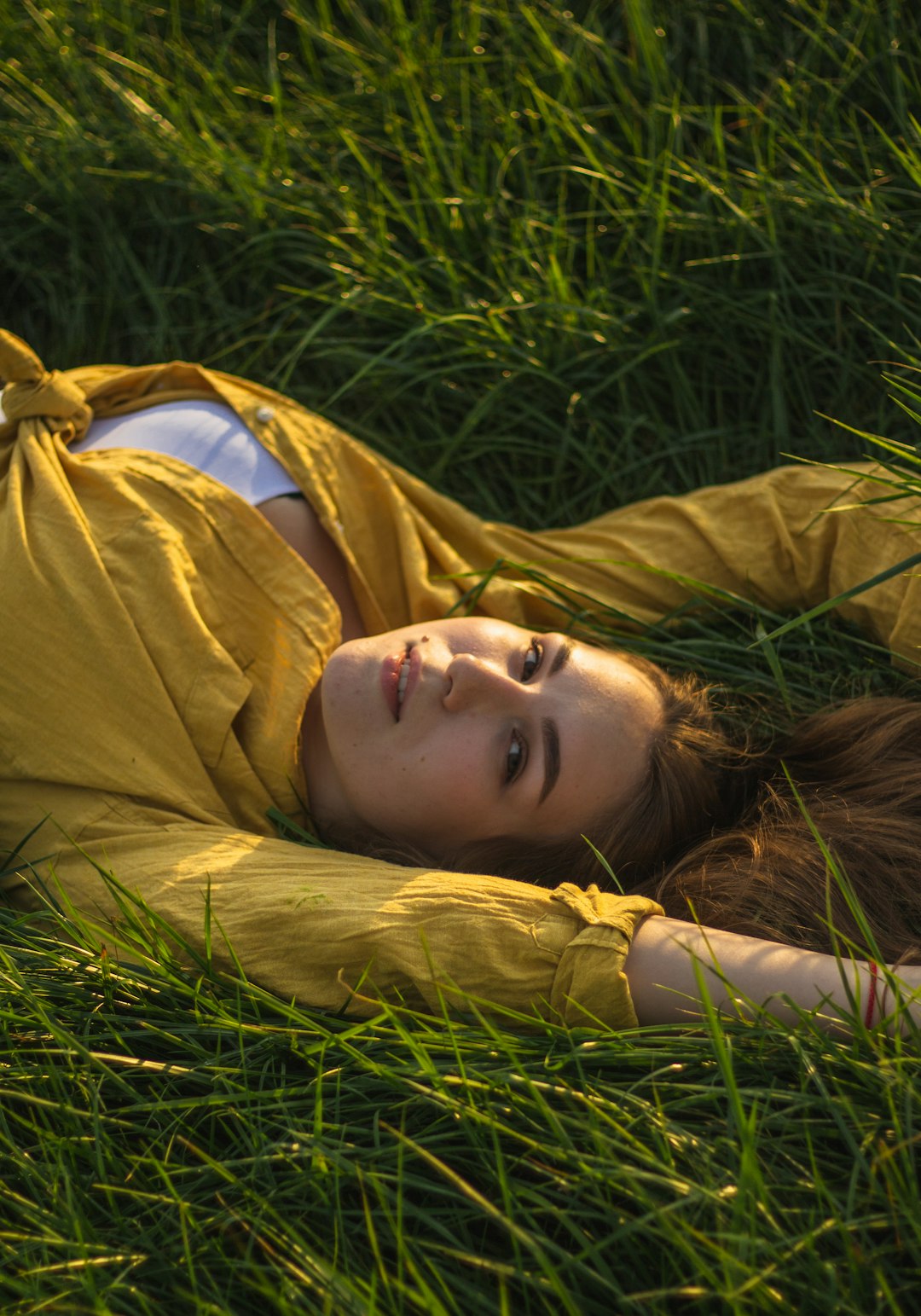 woman in brown coat lying on green grass during daytime