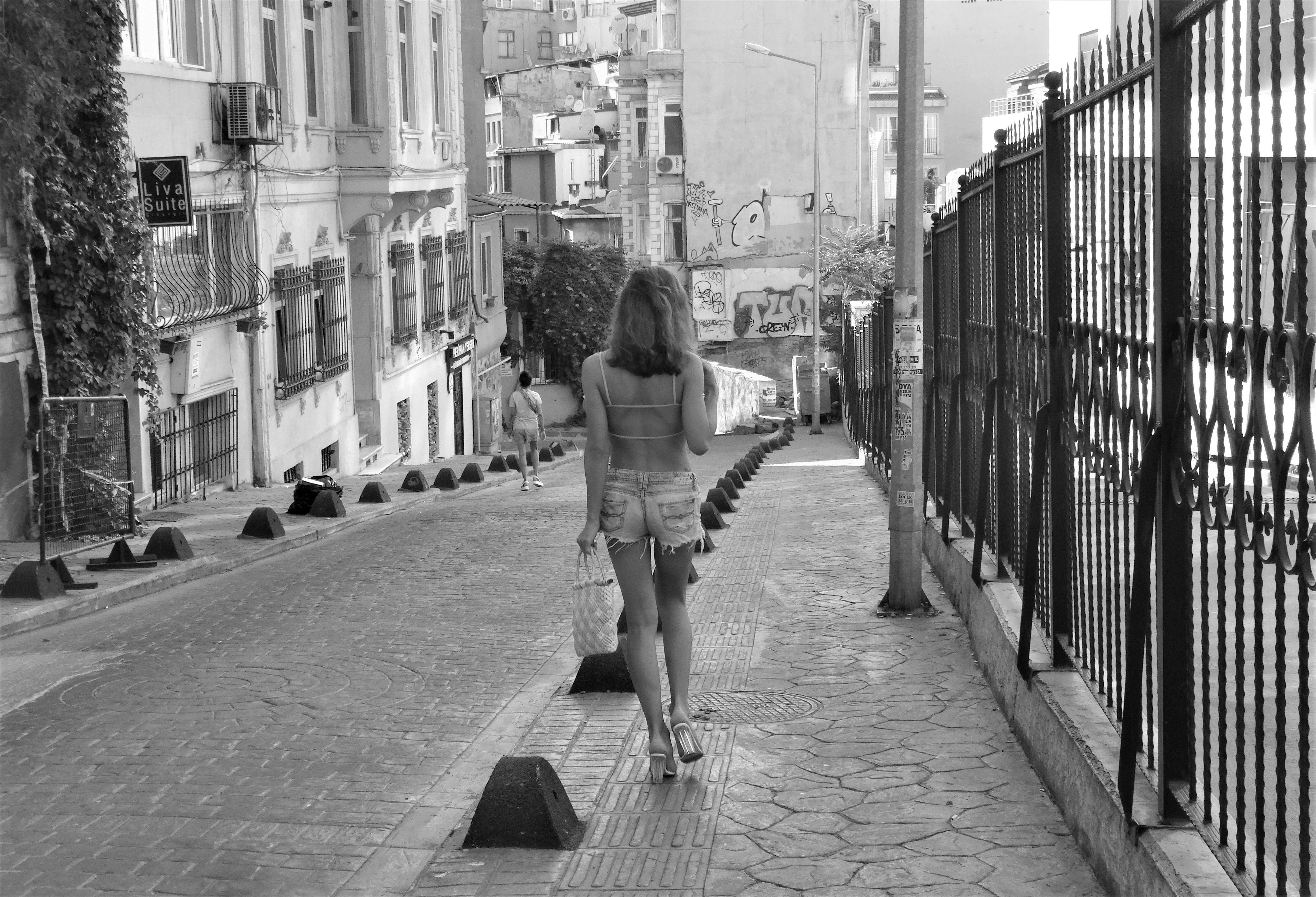 grayscale photo of woman walking on sidewalk