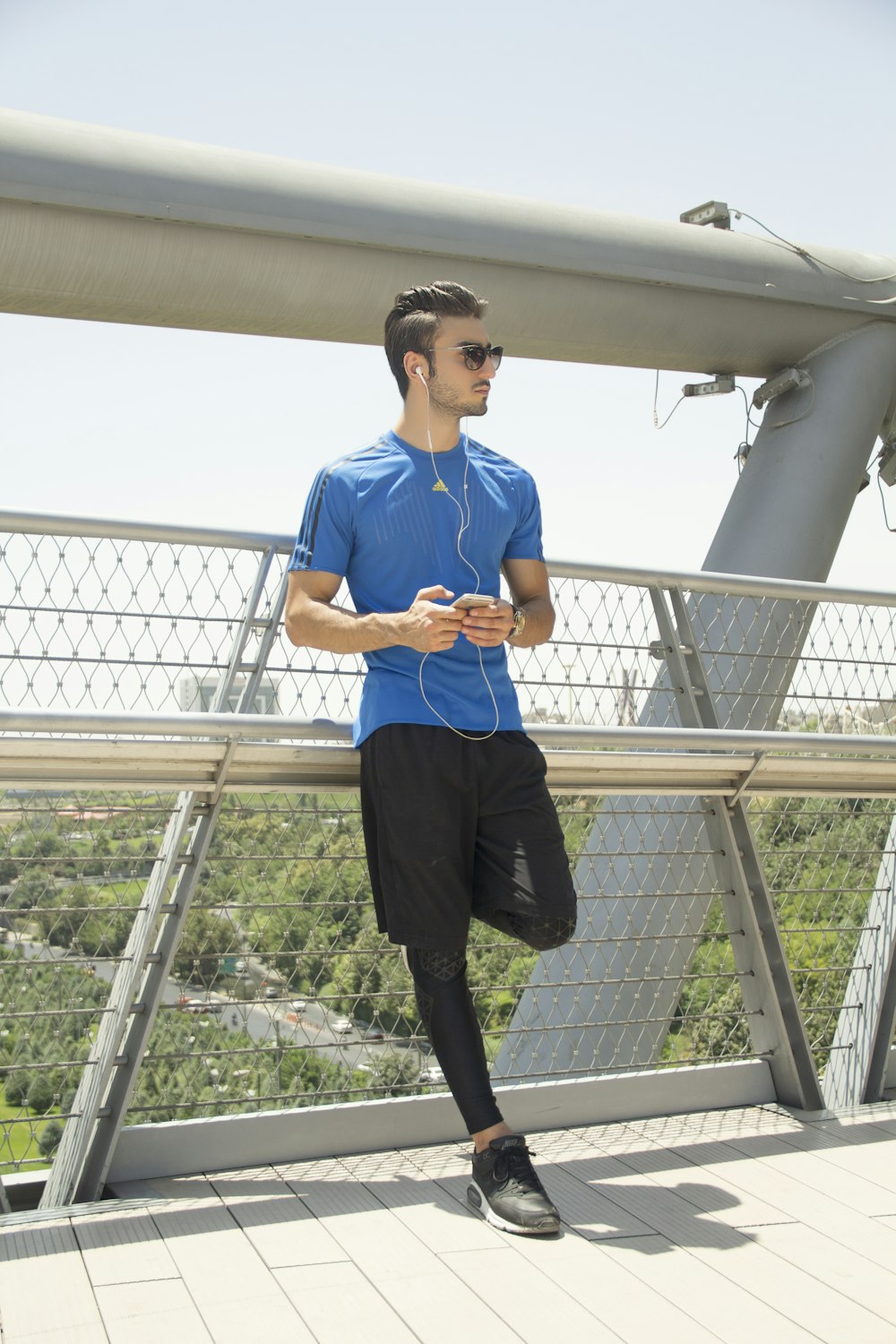 man in blue crew neck t-shirt and black pants standing on gray metal railings during