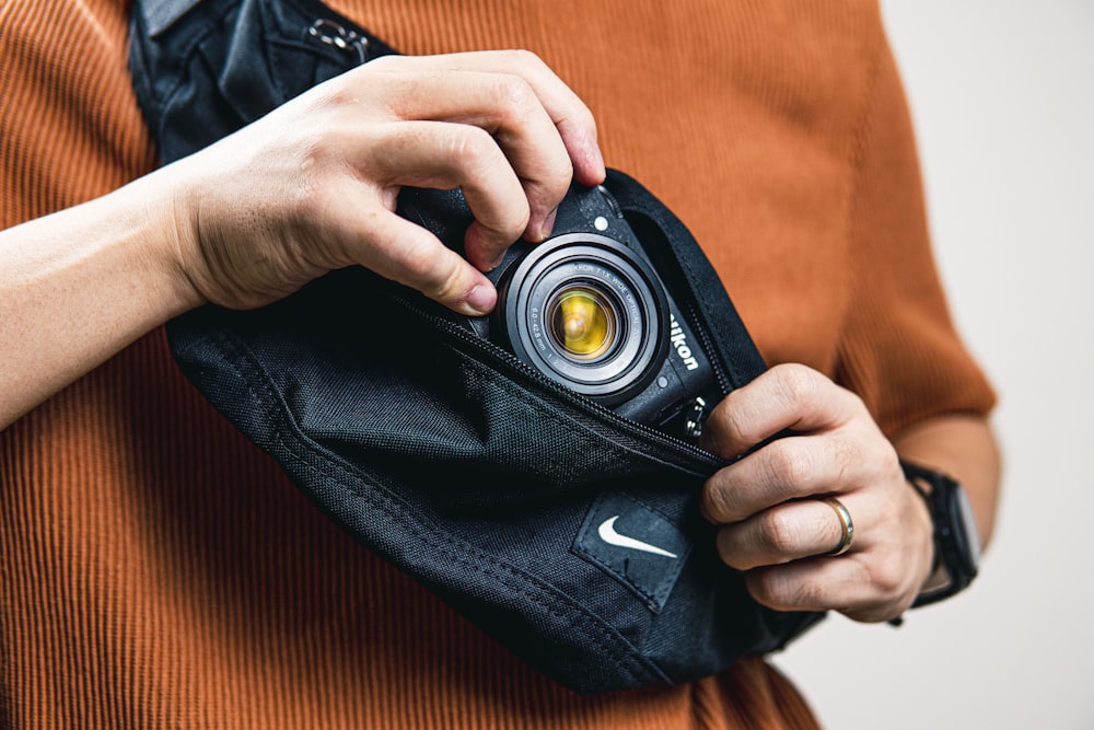 person holding black camera on orange textile