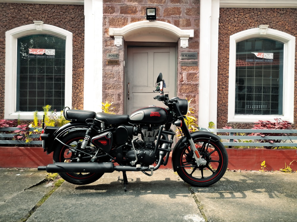 Motocicleta Cruiser negra y plateada estacionada junto a un edificio de concreto marrón durante el día