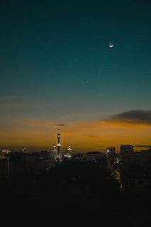 A crescent moon shining brightly over a mosque at dusk, symbolizing the start of a new Islamic month.